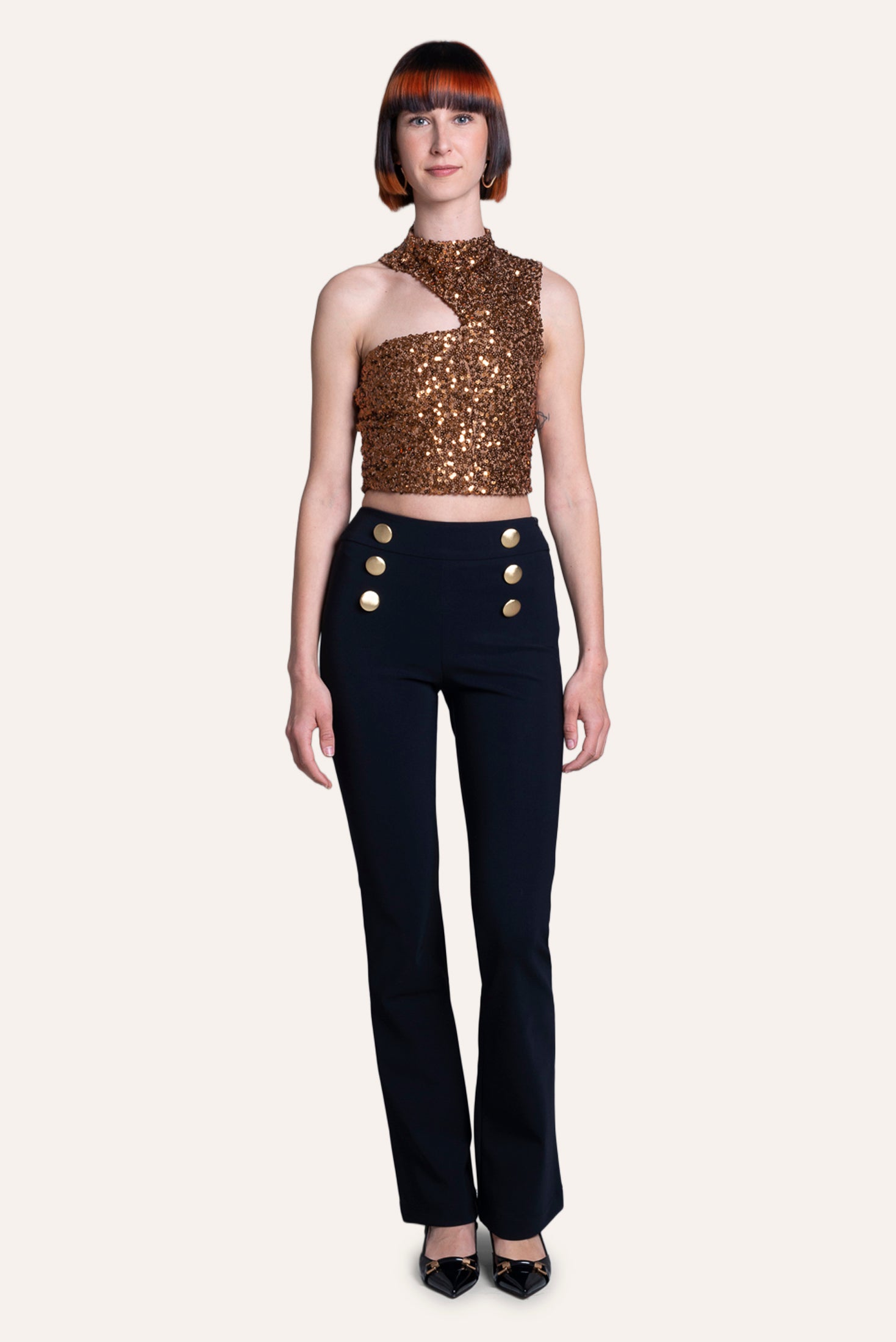Model wearing a gold sequin top and black pants with gold buttons on a white background