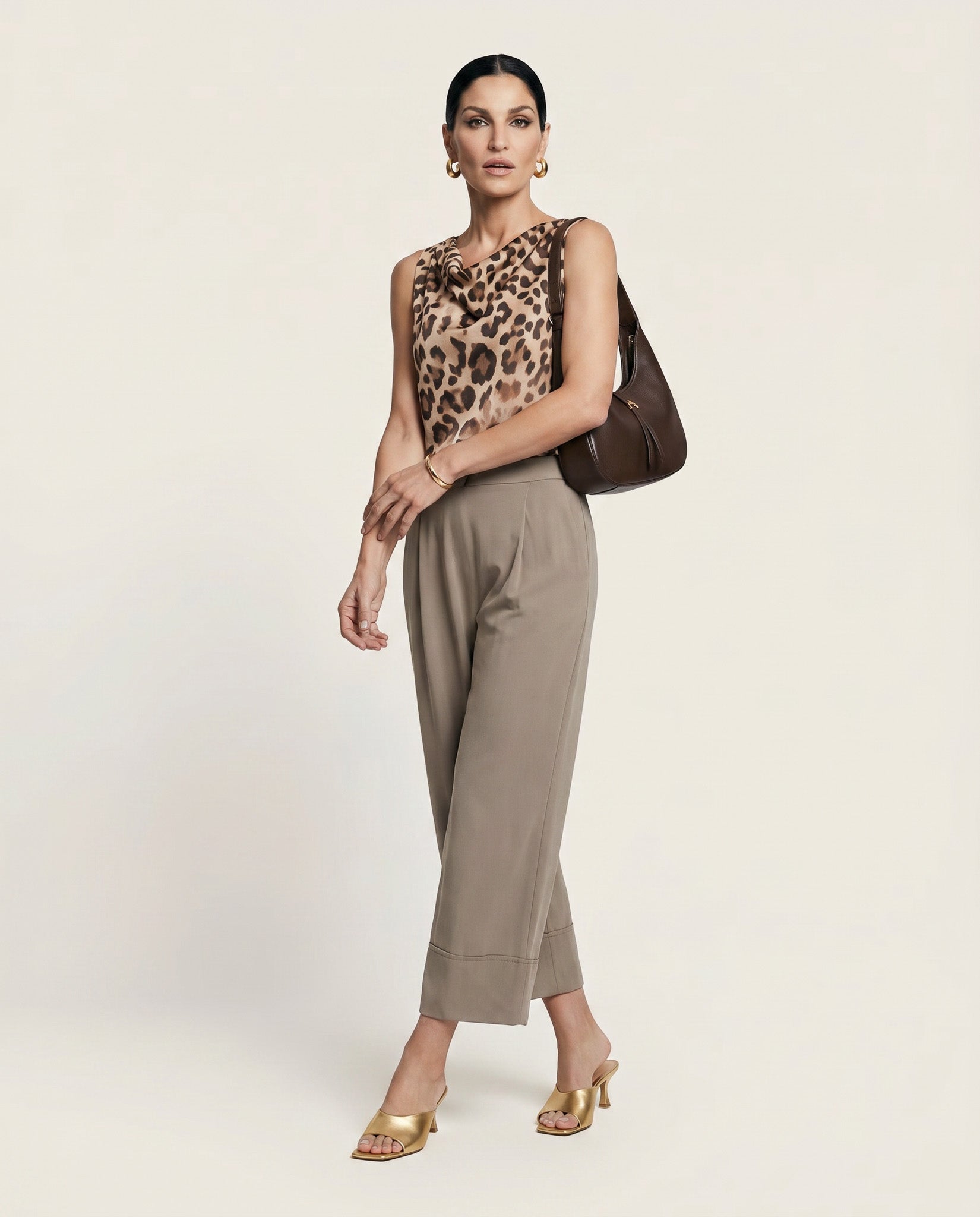 Woman wearing a leopard print top and beige pants with a brown handbag on a light background