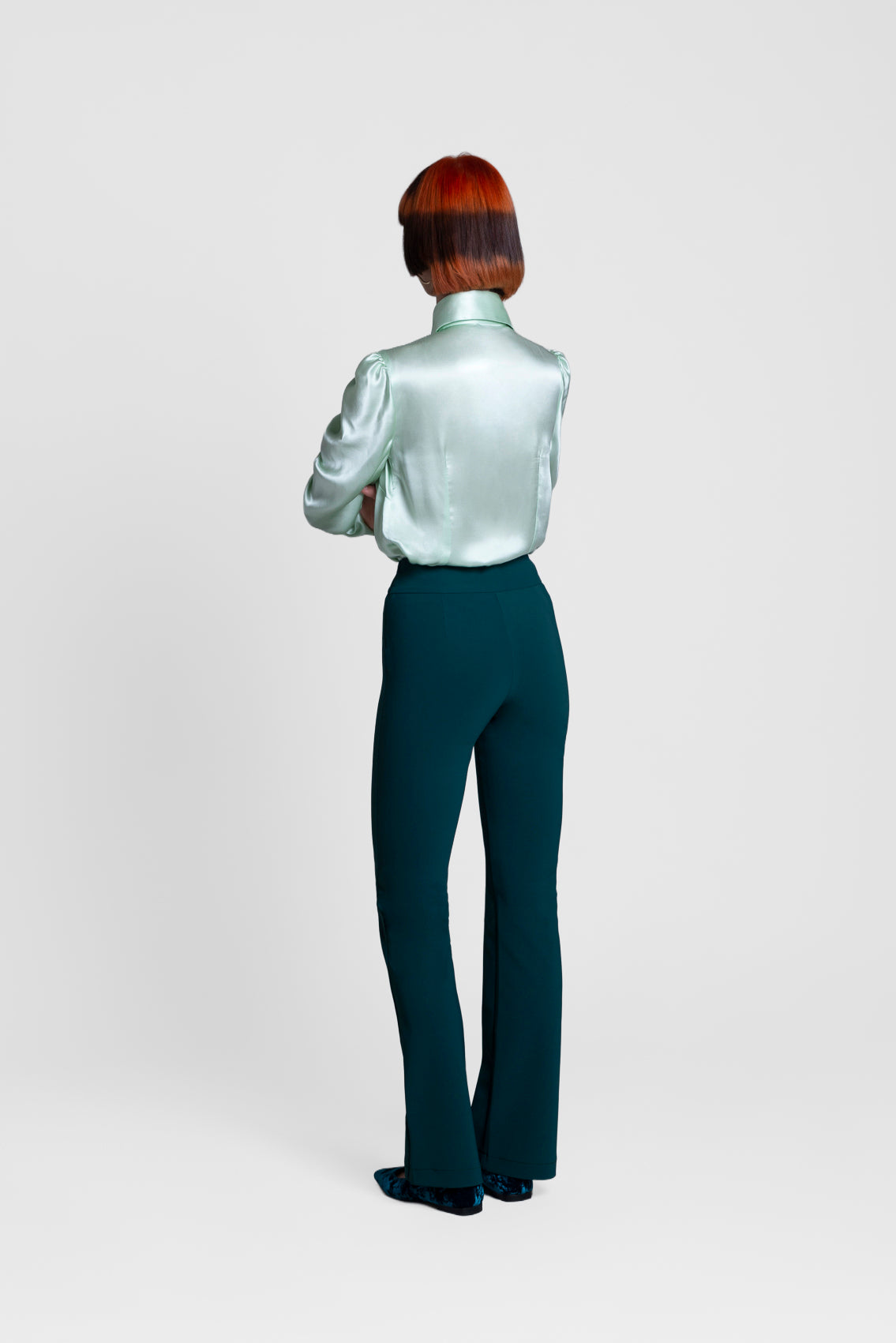 Person wearing a silver blouse and dark green pants on a light gray background