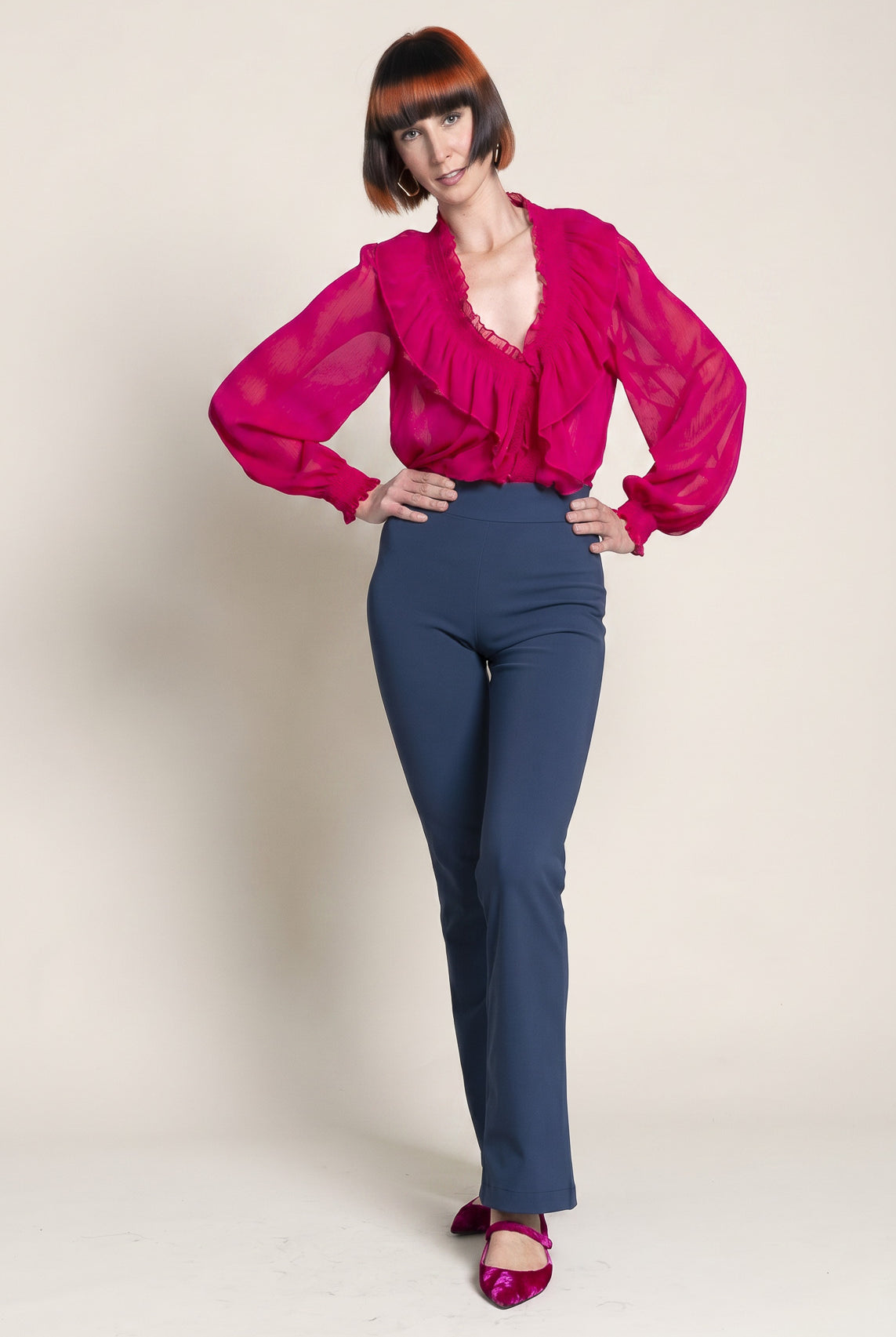 Person wearing a bright pink blouse and blue pants on a plain background