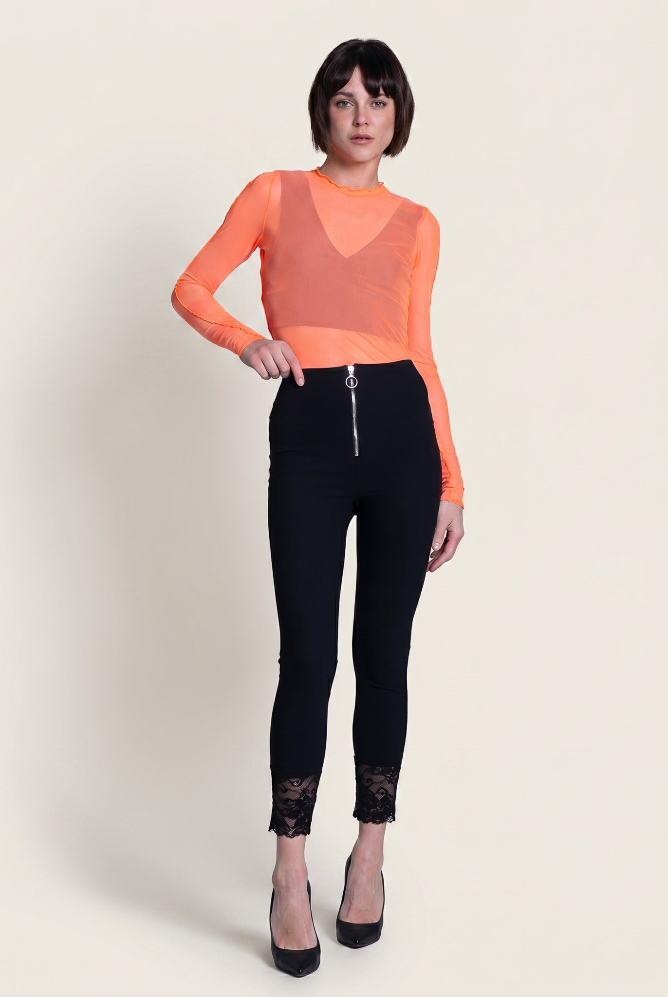 Woman wearing an orange sheer top and black pants on a white background