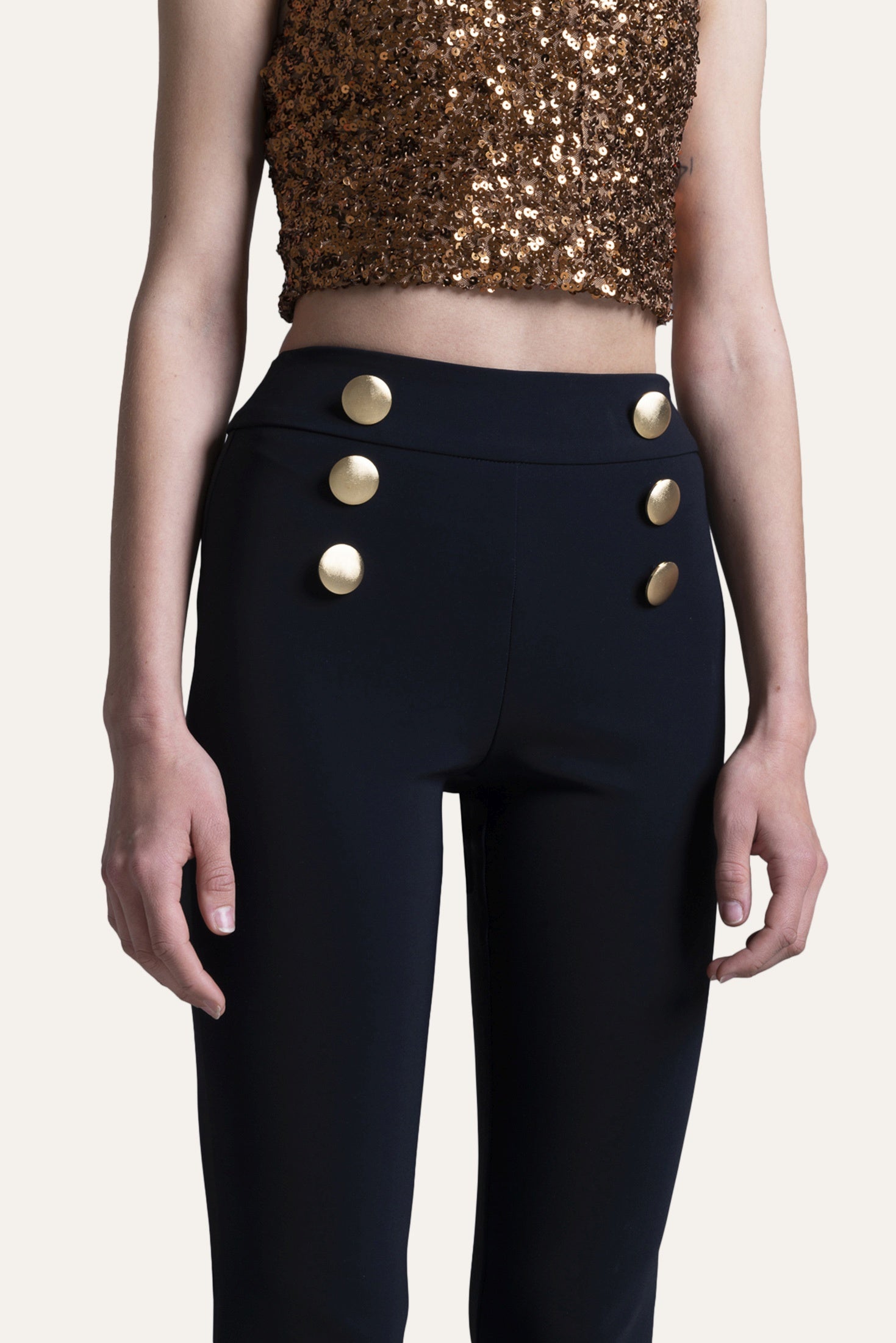 Black pants with gold buttons worn by a person on a white background