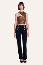 Model wearing a gold sequin top and black pants with gold buttons on a white background