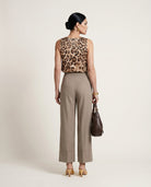 Woman wearing a leopard print top and beige pants with a brown handbag on a light background
