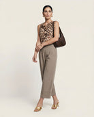 Woman wearing a leopard print top and beige pants with a brown handbag on a light background