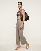 Woman wearing a leopard print top and beige pants, holding a brown handbag on a white background