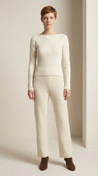 Woman wearing a cream ribbed sweater and pants with brown shoes on a neutral background