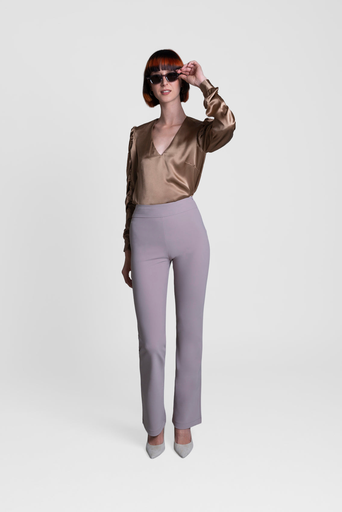 Person wearing a gold satin blouse and gray pants on a white background