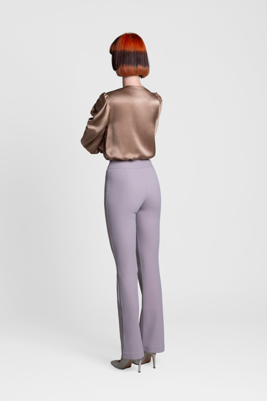 Person wearing a metallic blouse and beige pants on a white background