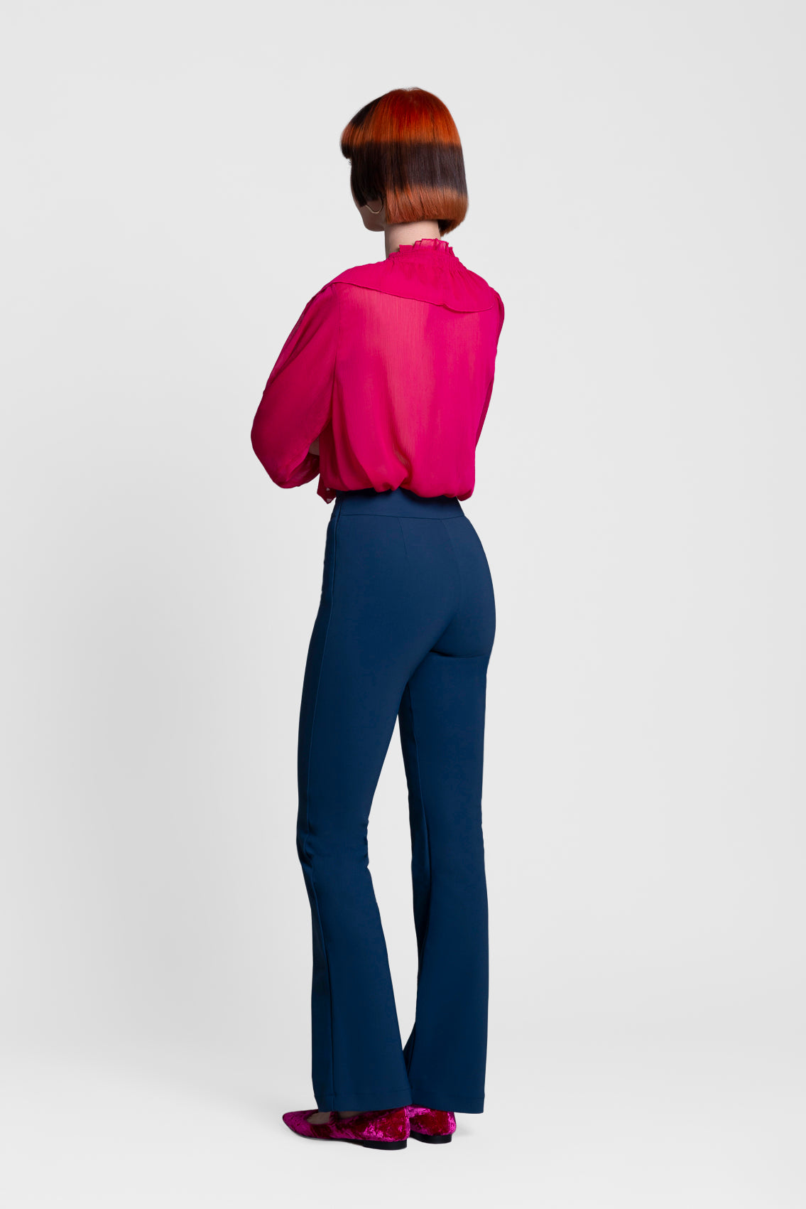 Model wearing a bright pink blouse and blue pants on a white background