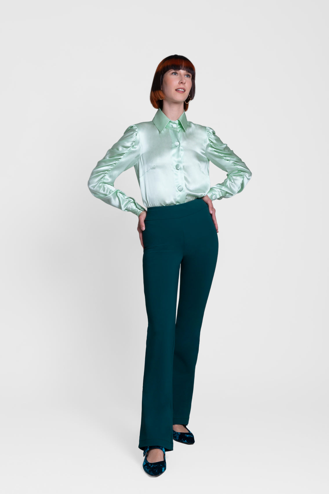 Person wearing a light green satin shirt and dark green pants on a white background