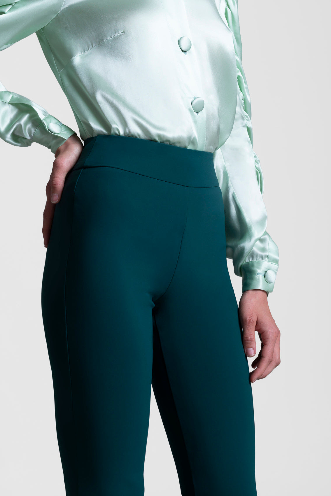 Person wearing a light green satin shirt and dark green pants on a plain background