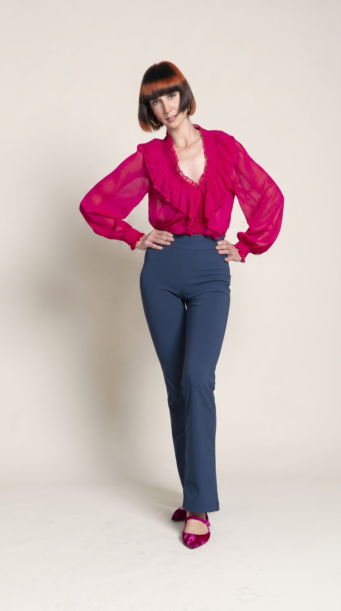 Person wearing a bright pink blouse and blue pants on a plain background