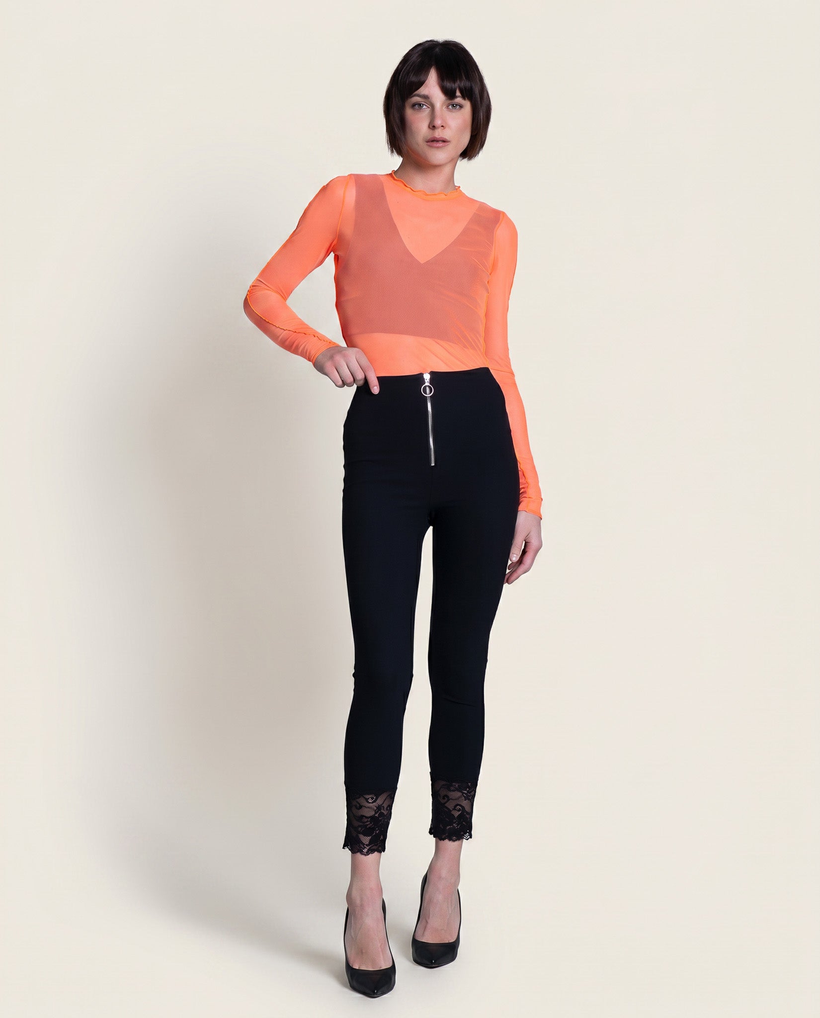 Woman wearing an orange sheer top and black pants on a white background